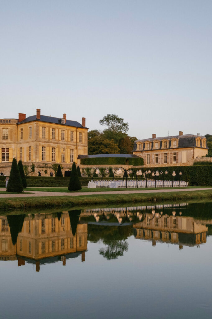 Chateau, gardens, and pond at sunset with elegant wedding setup.