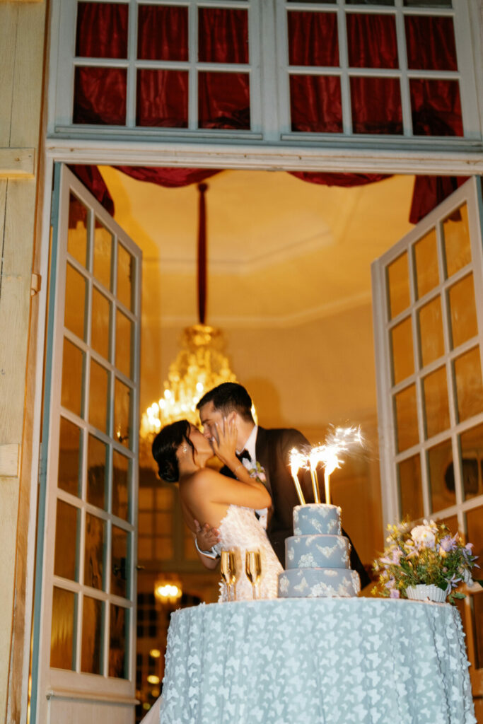 Bride and groom kiss by sparkler cake, elegant decor.