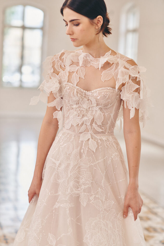 Woman in elegant lace wedding dress with cape indoors.