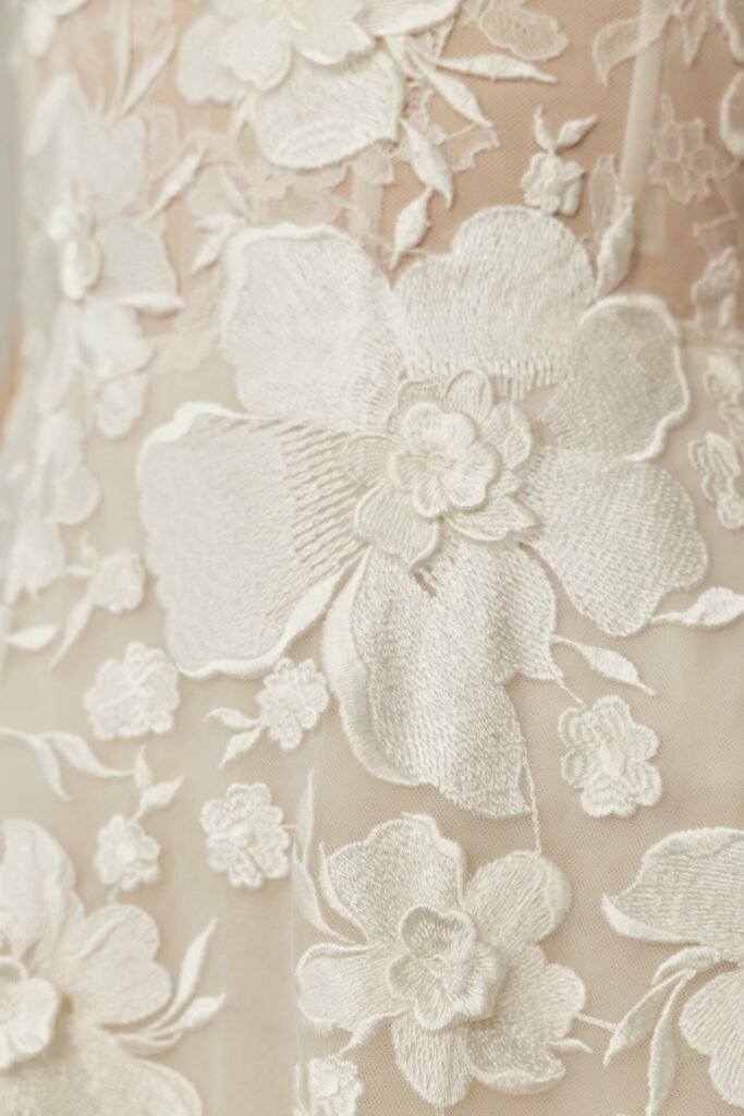Sheer beige fabric with white embroidered floral patterns.