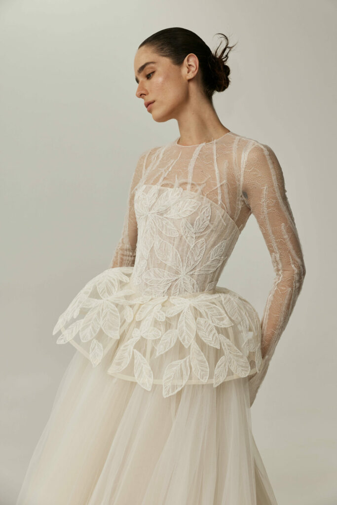 Woman in sheer embroidered white wedding dress, low bun.