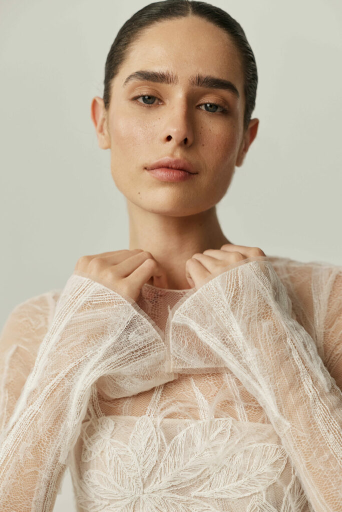 Person in sheer embroidered top, confidently holding collar.