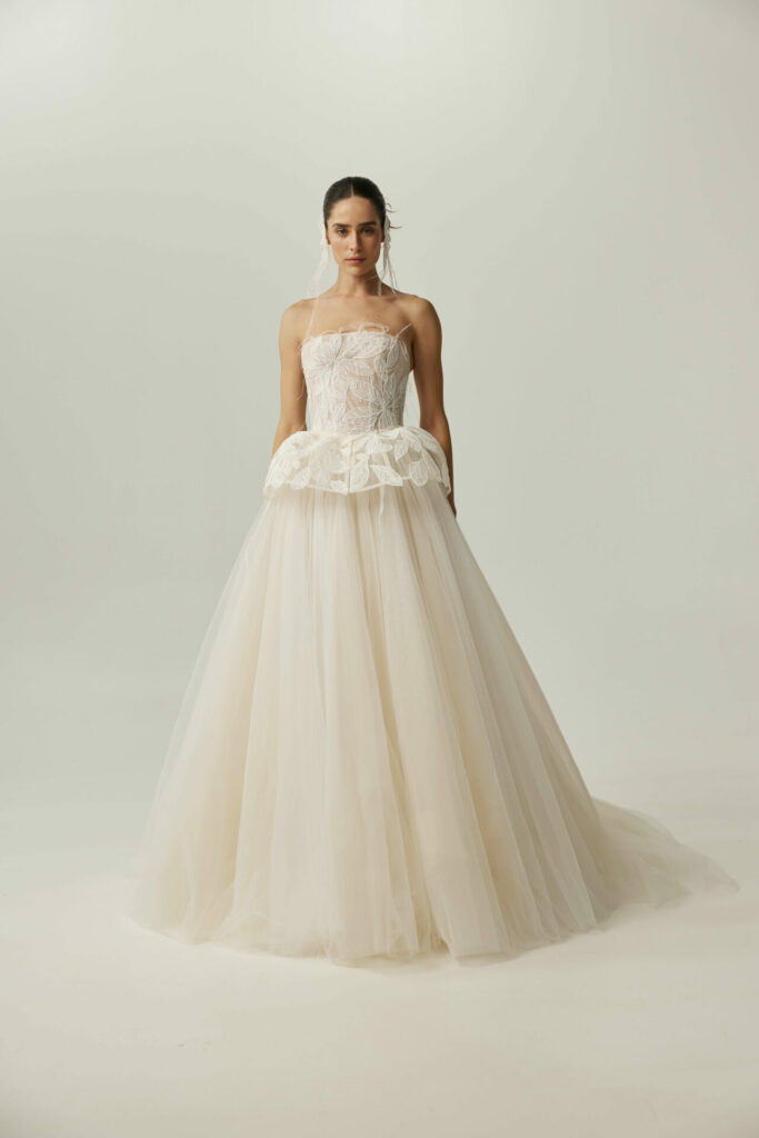 Woman in strapless white lace ball gown, plain background.