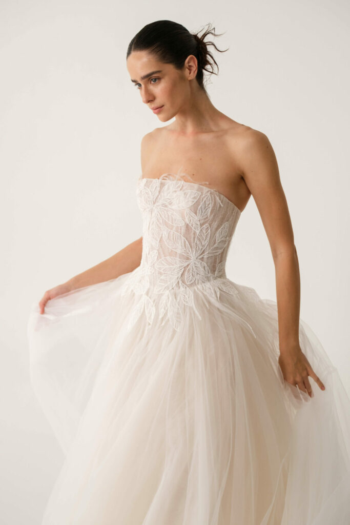 Bride in white strapless gown holds skirt softly.