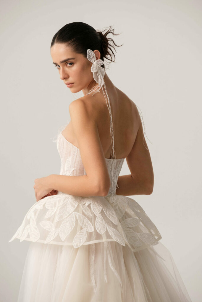 Woman in white leaf dress, hair back, floral earpiece.