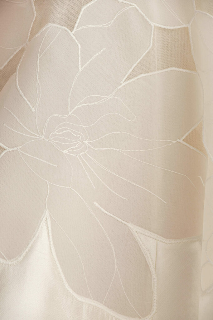Cream sheer fabric with white floral stitching, elegant.