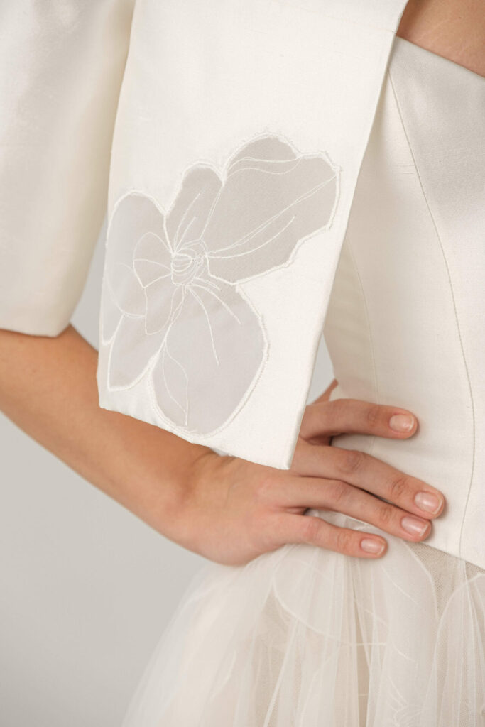 Elegant white Loie dress, floral sleeve, hand on waist.