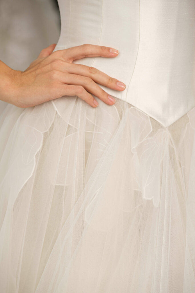 Hand on white satin dress with floral details.