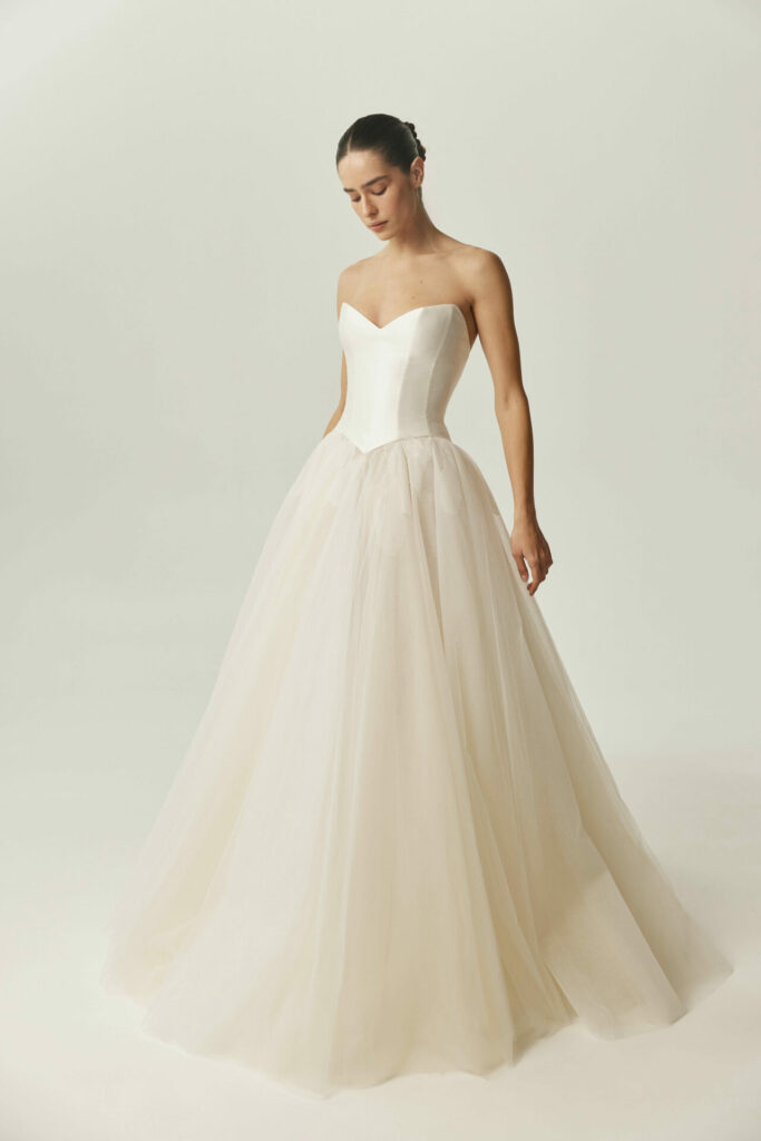 Woman in strapless ivory gown looks down, elegant.