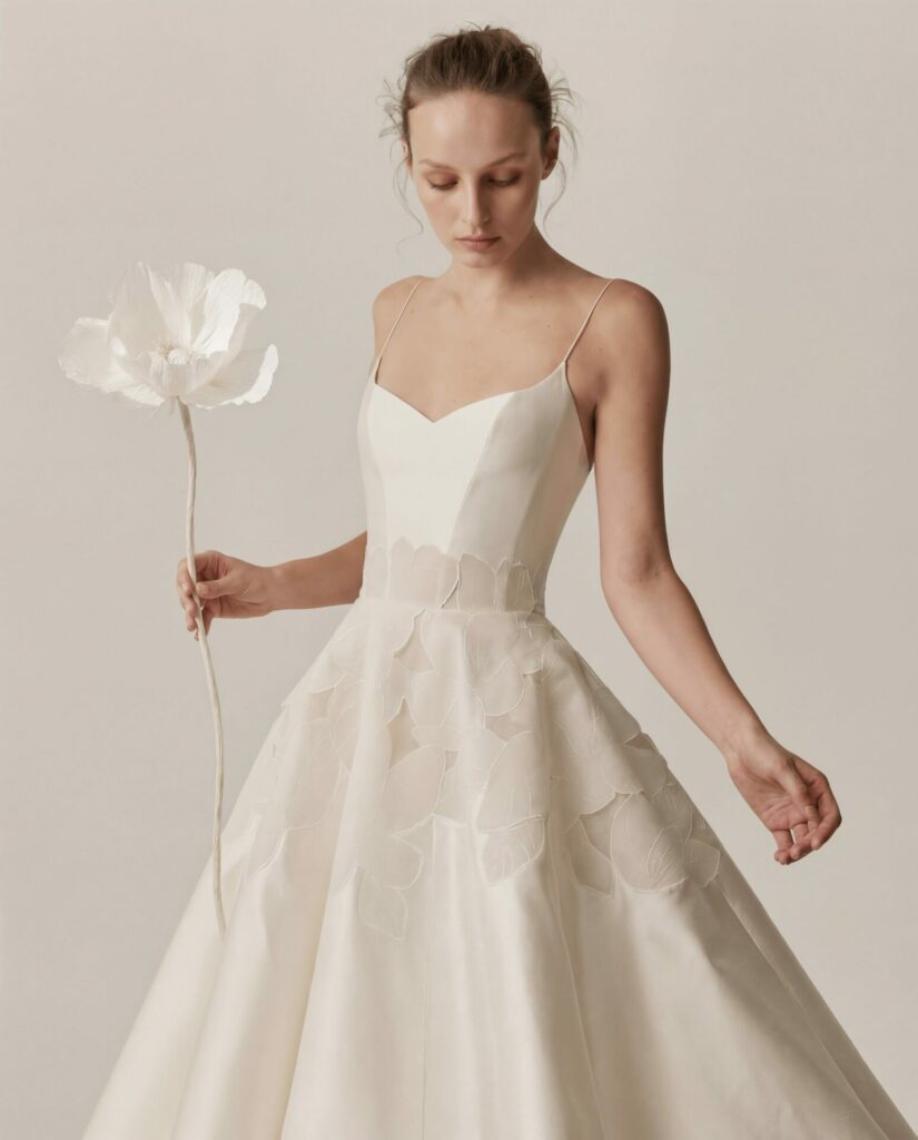 Serina in leaf-appliqué wedding dress, holding paper flower.