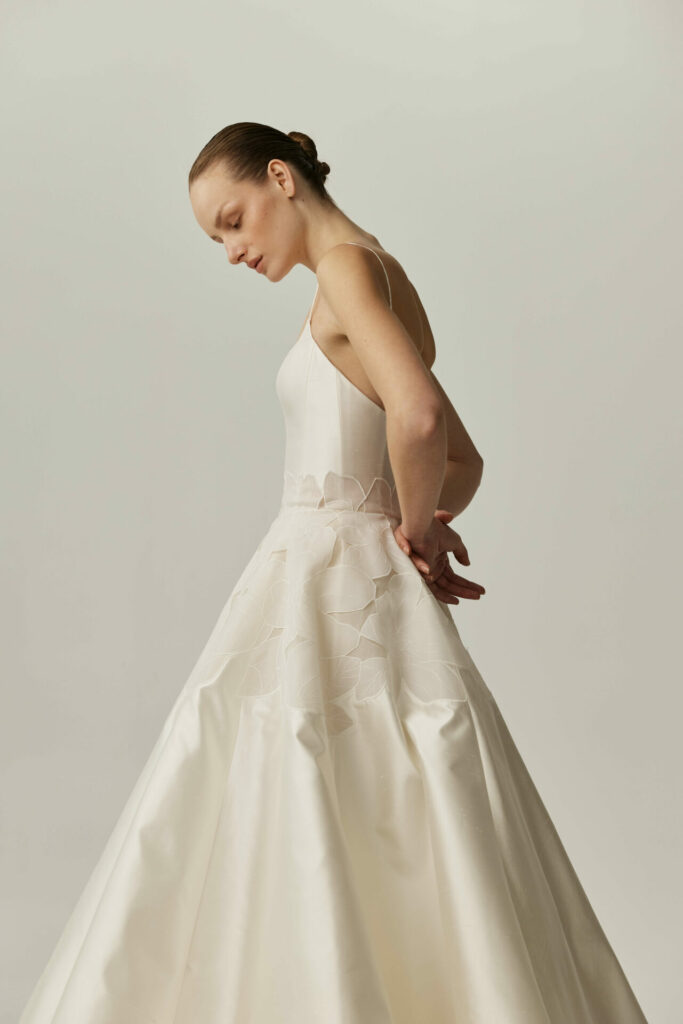Serina in white floral dress, standing sideways, looking down.