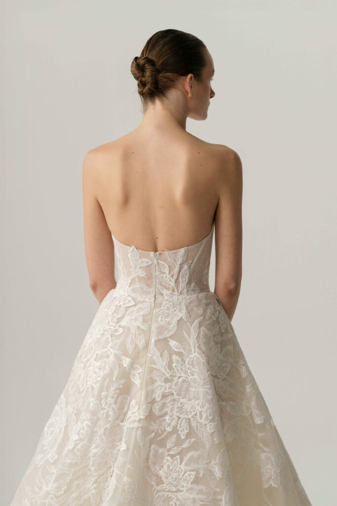 Woman in white lace wedding gown, low bun, back view.