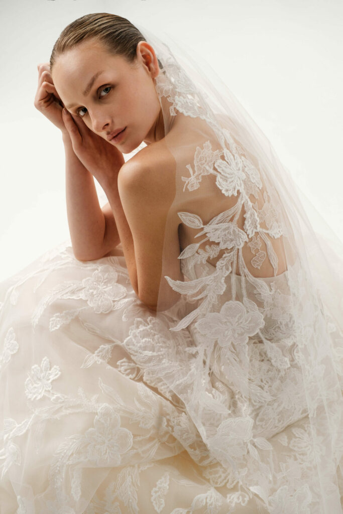 Woman in white floral lace Sui wedding dress seated.