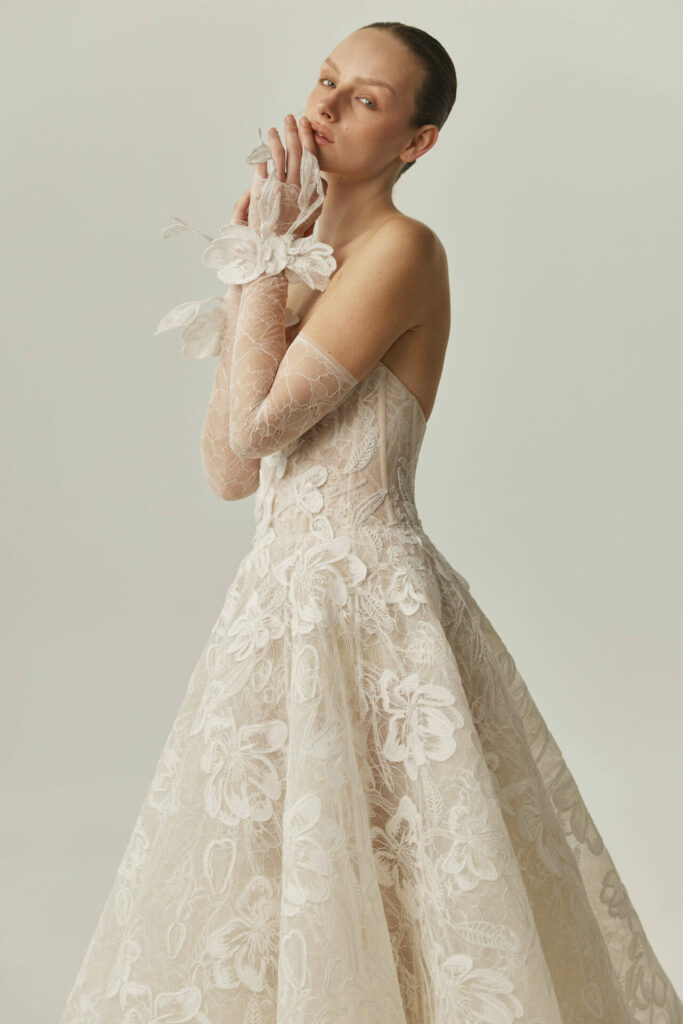 Woman poses in white lace gown and floral gloves.