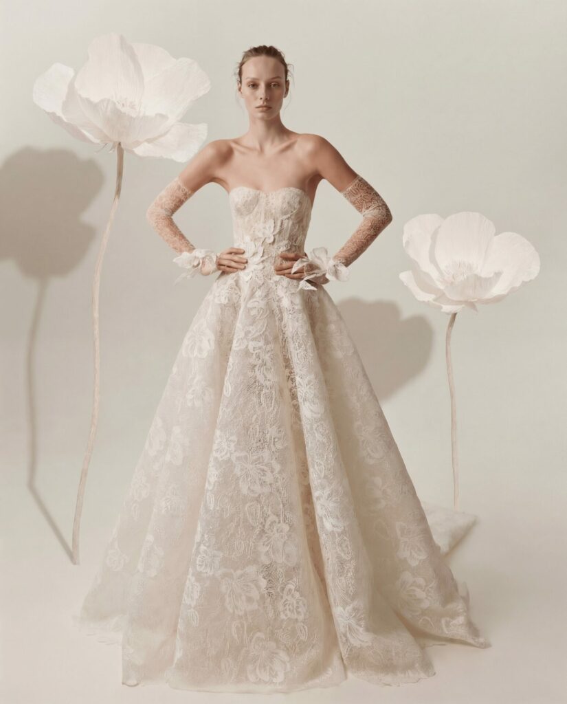Woman in lace wedding gown among white paper flowers.