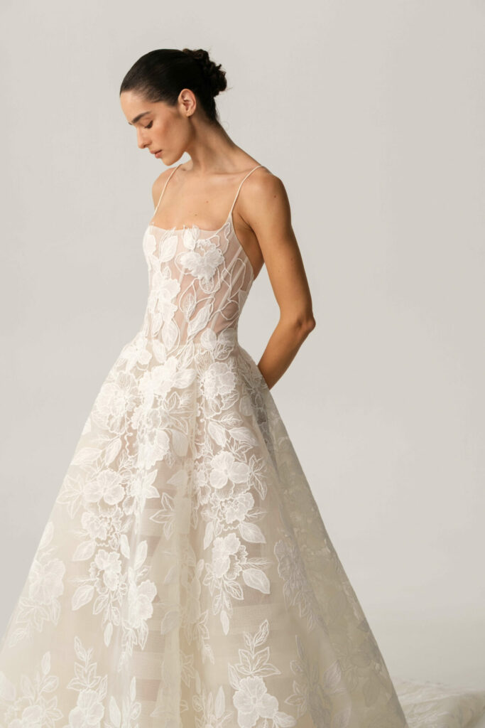 Woman in lace wedding gown looks down, hands back.
