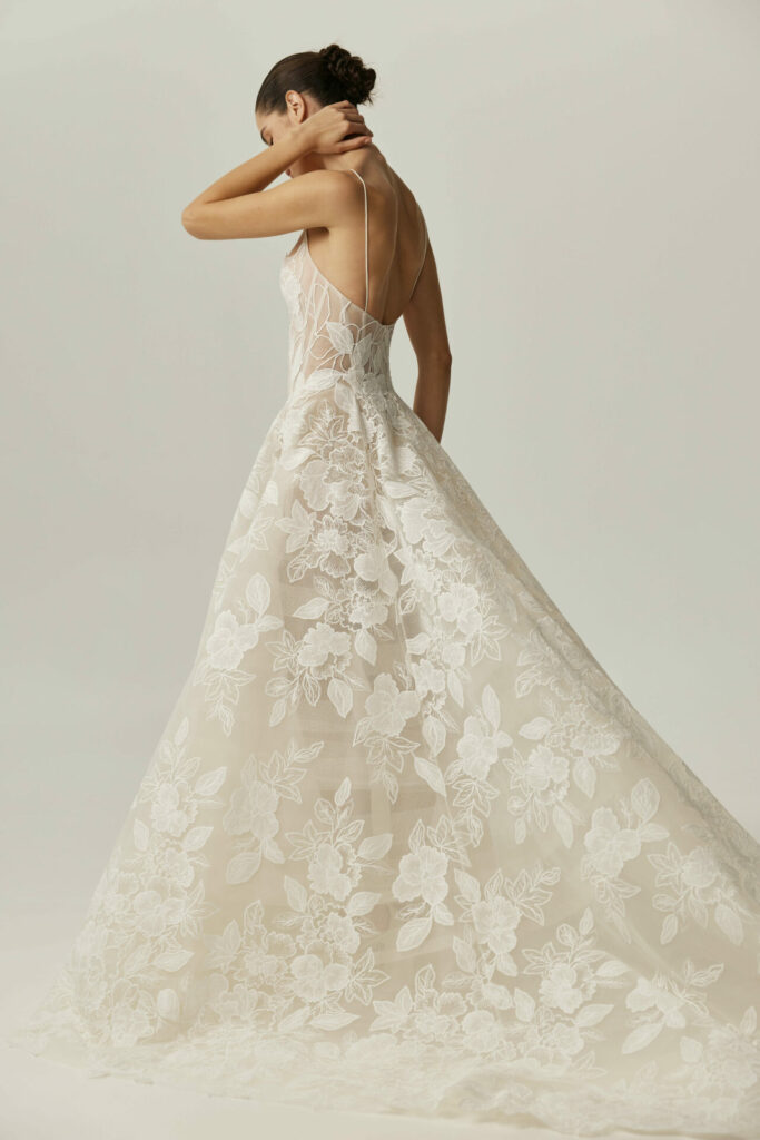 Woman in lace wedding gown with low bun touching neck.