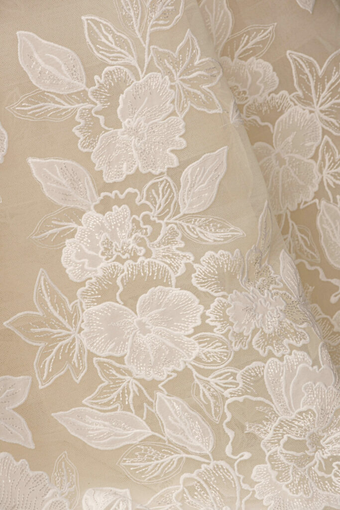 Beige fabric with detailed white floral lace embroidery.