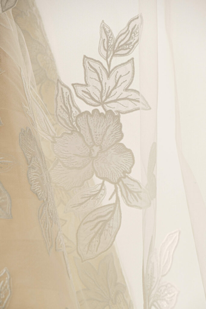Sheer white fabric, large floral embroidery, elegantly draped.