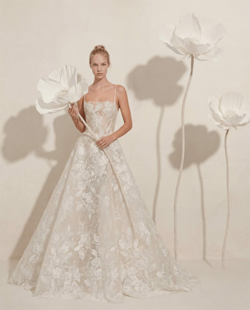 Woman in floral lace gown holds white paper flower.