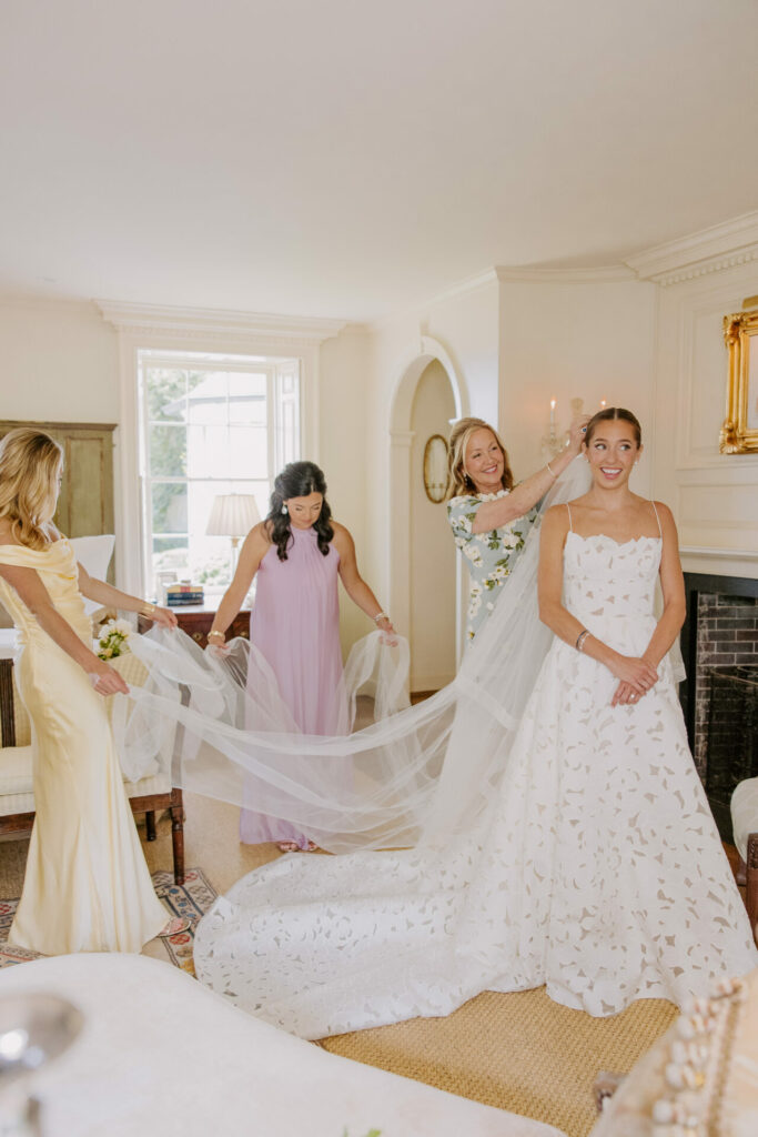 Bride and women adjust her veil in elegant room.