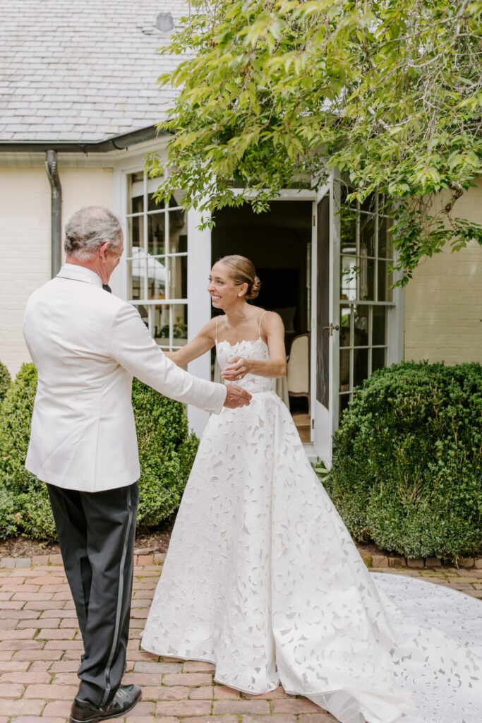 Bride in luxury gown smiles, arms outstretched to man.