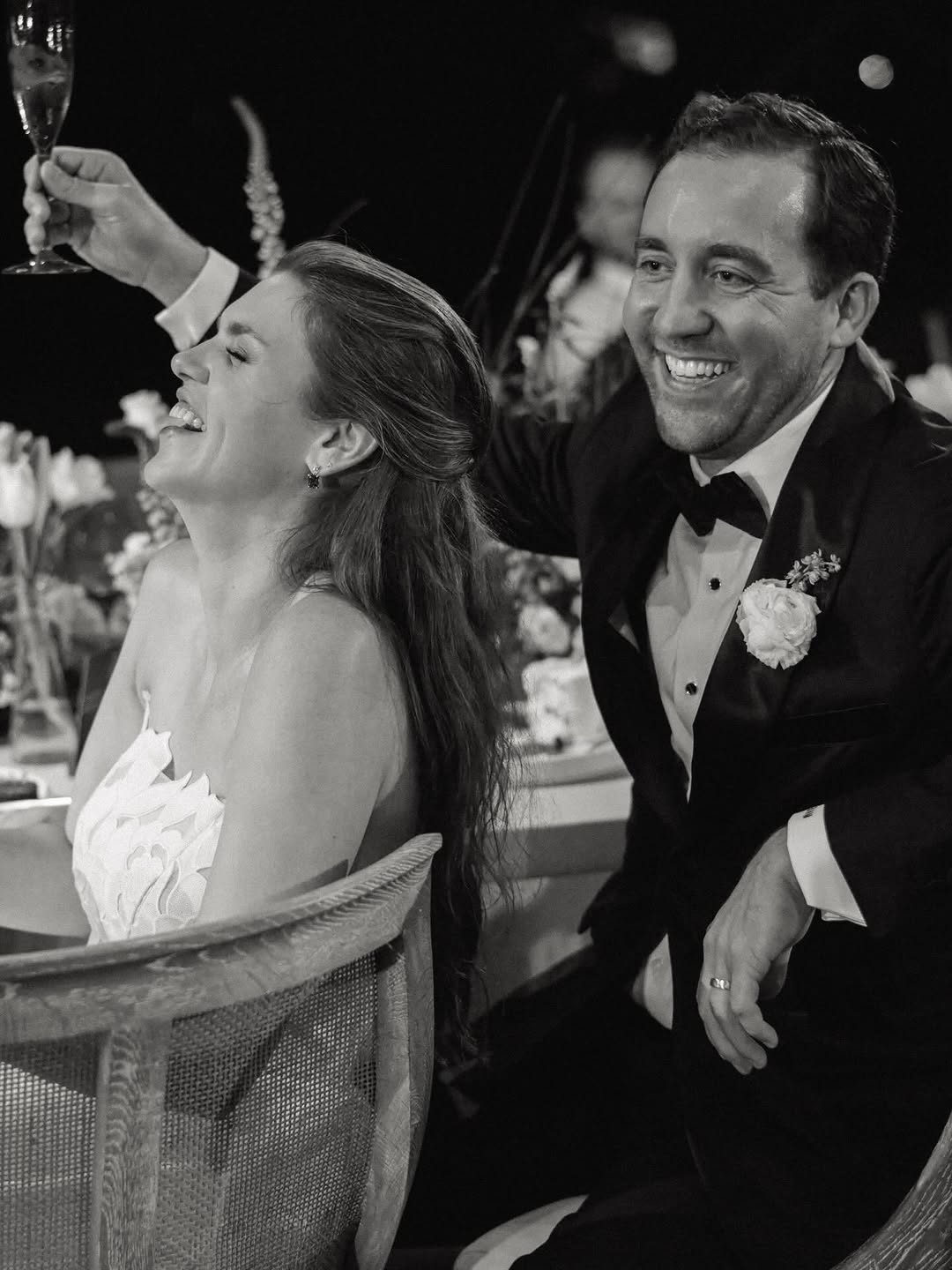 Bride and groom laughing, toasting at elegant reception.