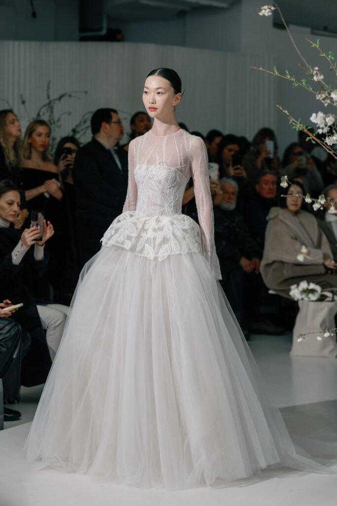 Model in sheer lace wedding dress on runway.