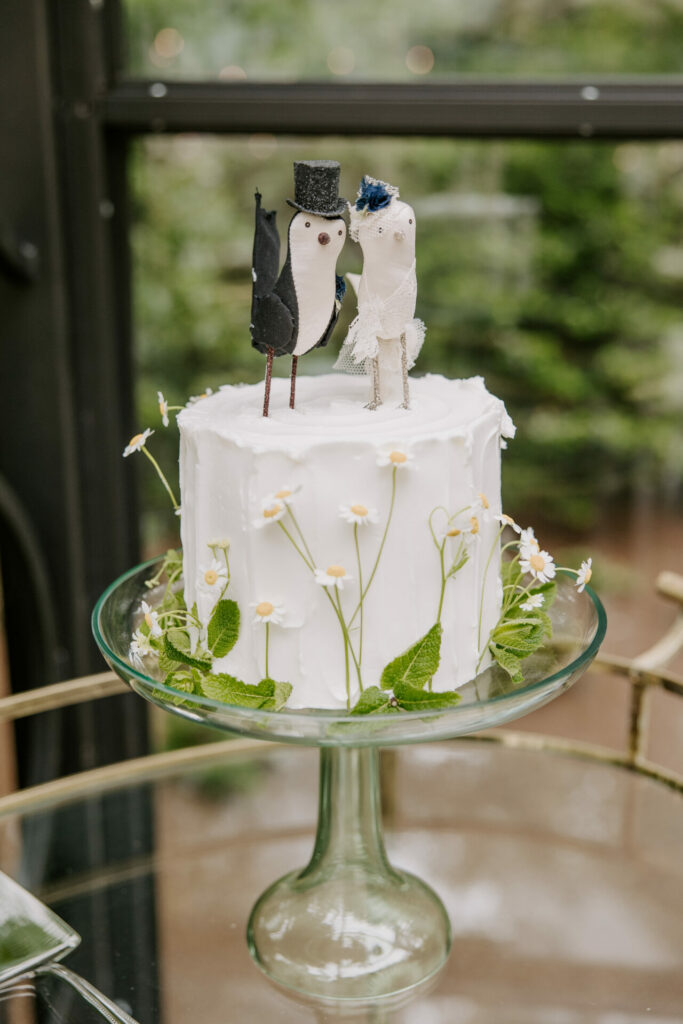 Cake with wedding bird toppers, white flowers, greenery.