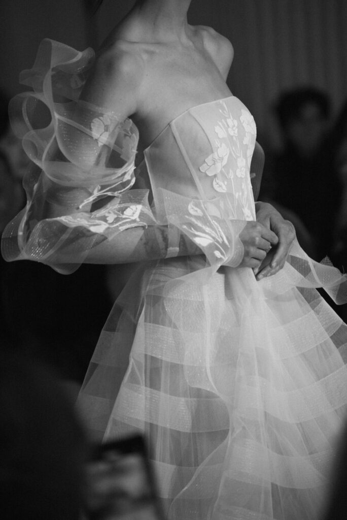 Mira Zwillinger SS2027 Clea wedding dress with sheer floral lace bodice, black and white editorial.