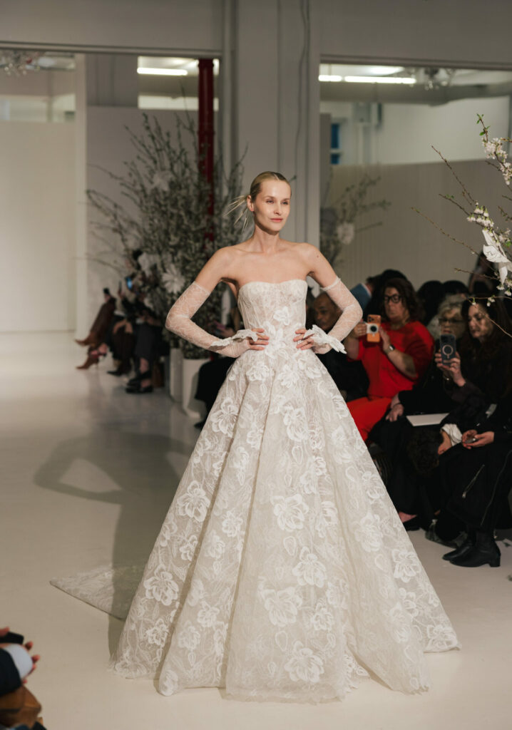 Model in strapless lace Clea gown walks runway.