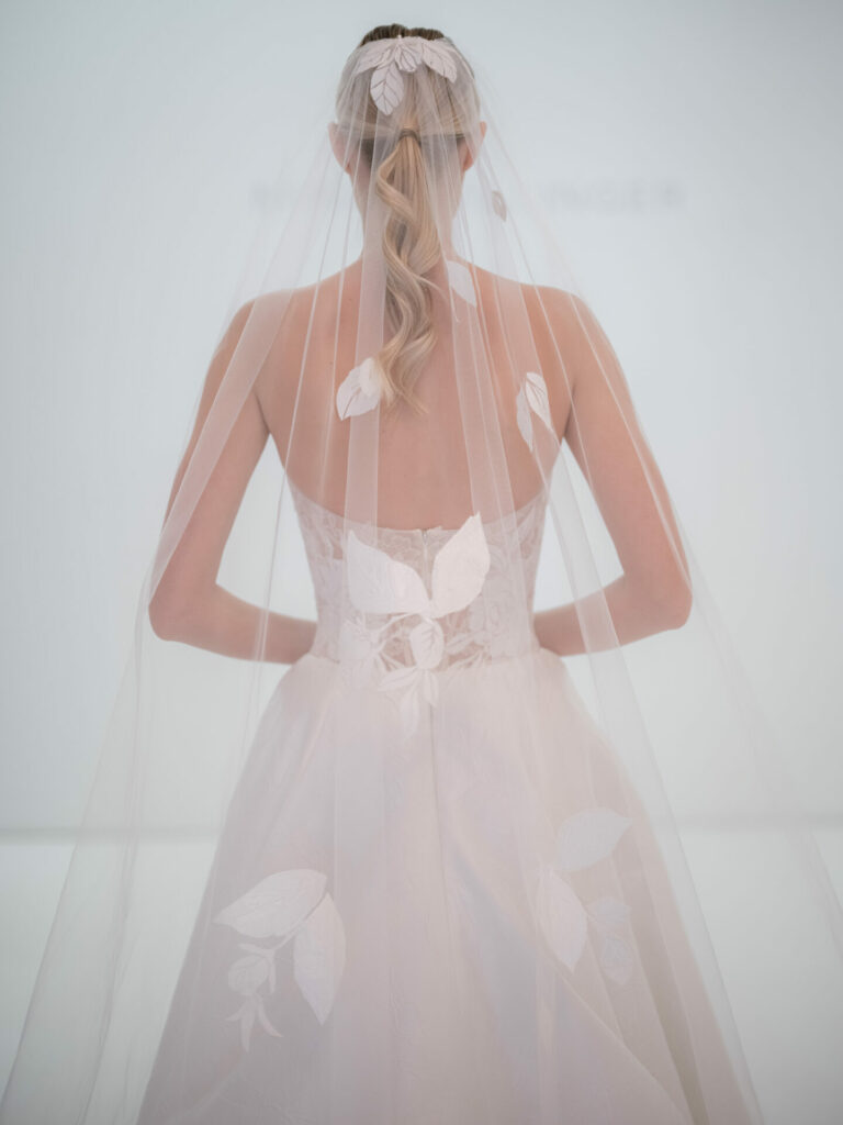 Bride in strapless dress, sheer leaf veil, ponytail.