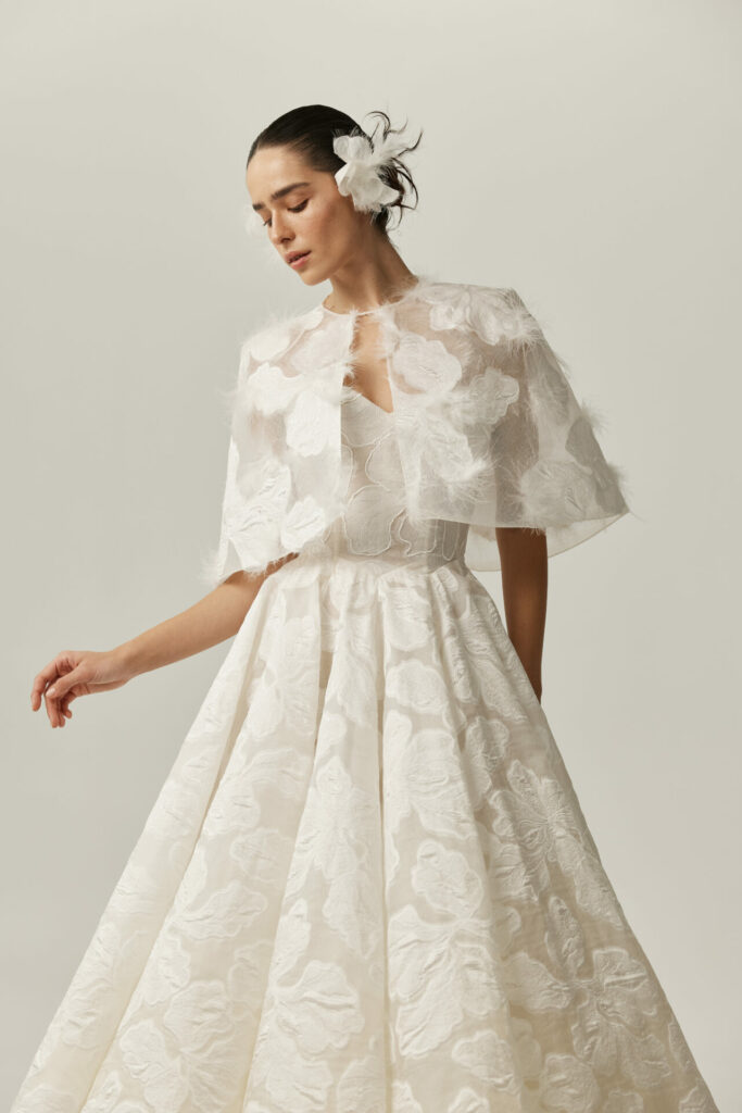 Woman poses in white Clea dress, flower hair accessory.