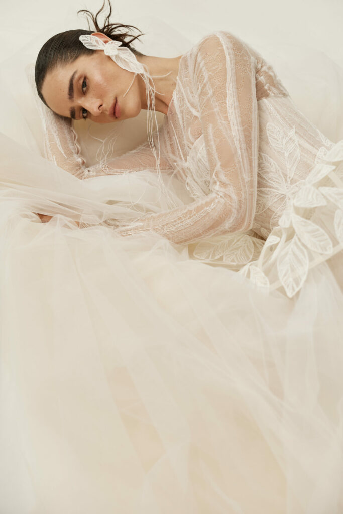 Woman in sheer leaf-patterned gown reclines, feather earring.