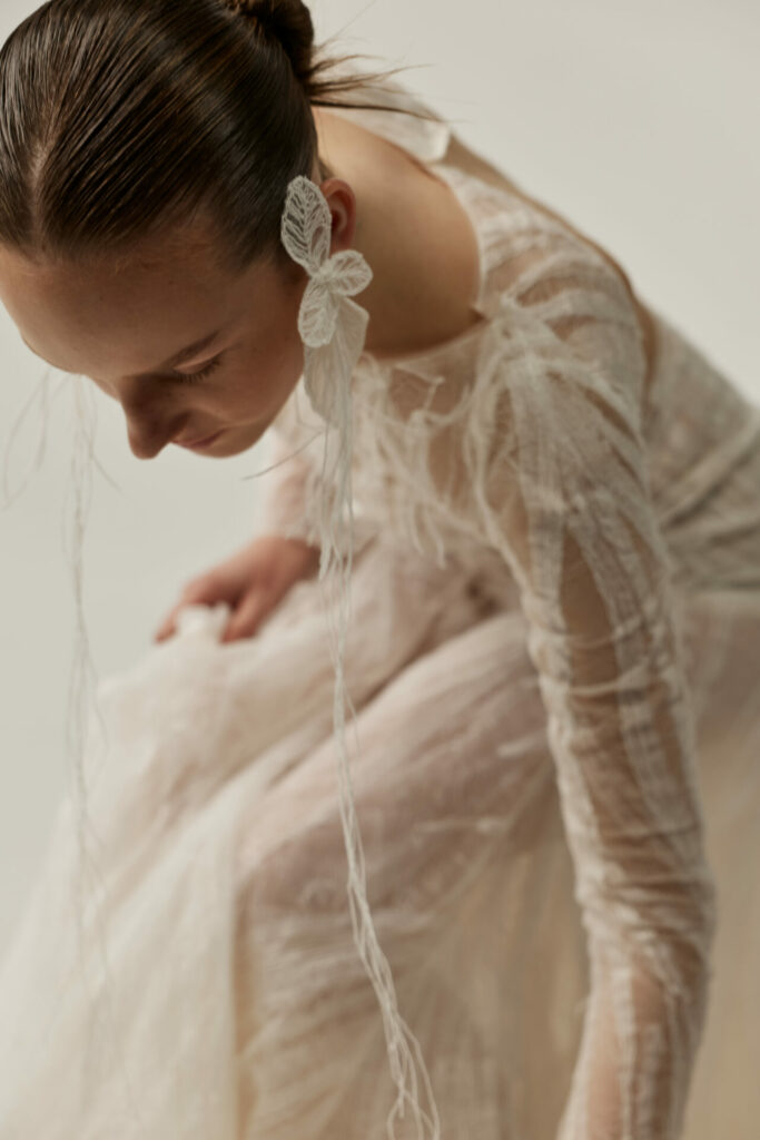 Woman leans in sheer white dress, lace earring.