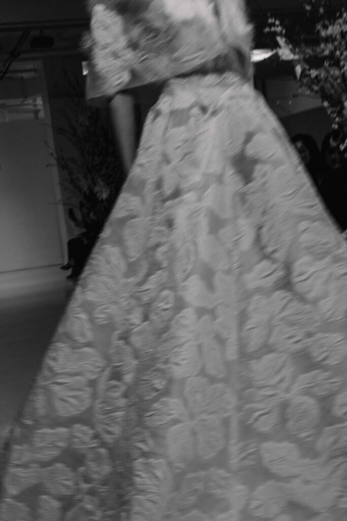 Blurred black-and-white runway photo of floral Clea wedding dress.