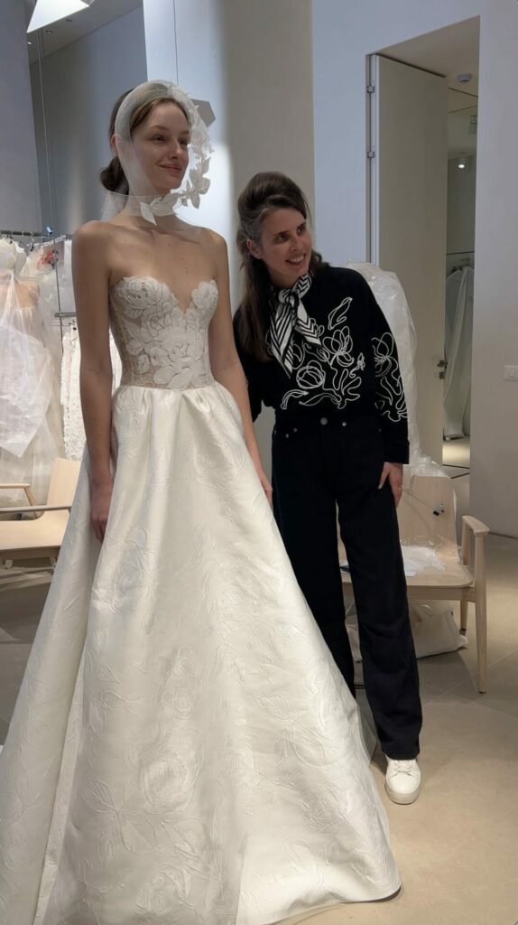 Designer smiles beside model in floral Clea gown.