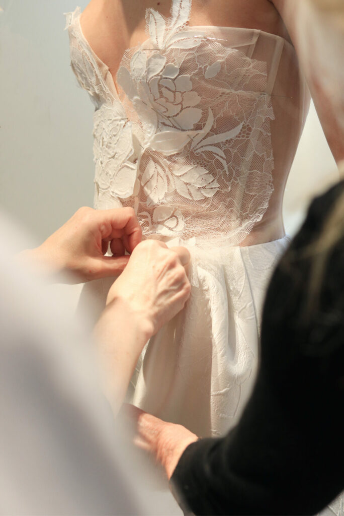 Hands adjust Clea wedding dress with lace detail.