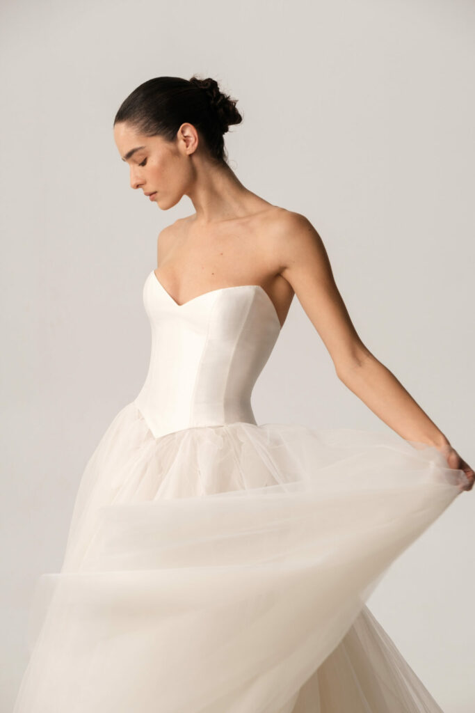 Woman in strapless Clea gown holds skirt gracefully.