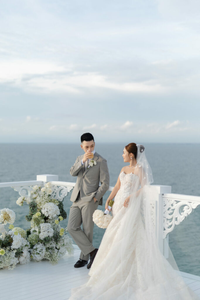 Bride and groom on oceanfront balcony, white florals.