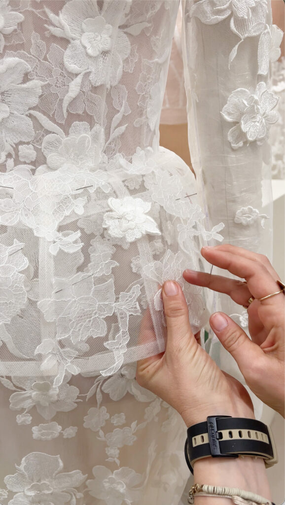 Hands adjusting floral lace fabric on dress form.