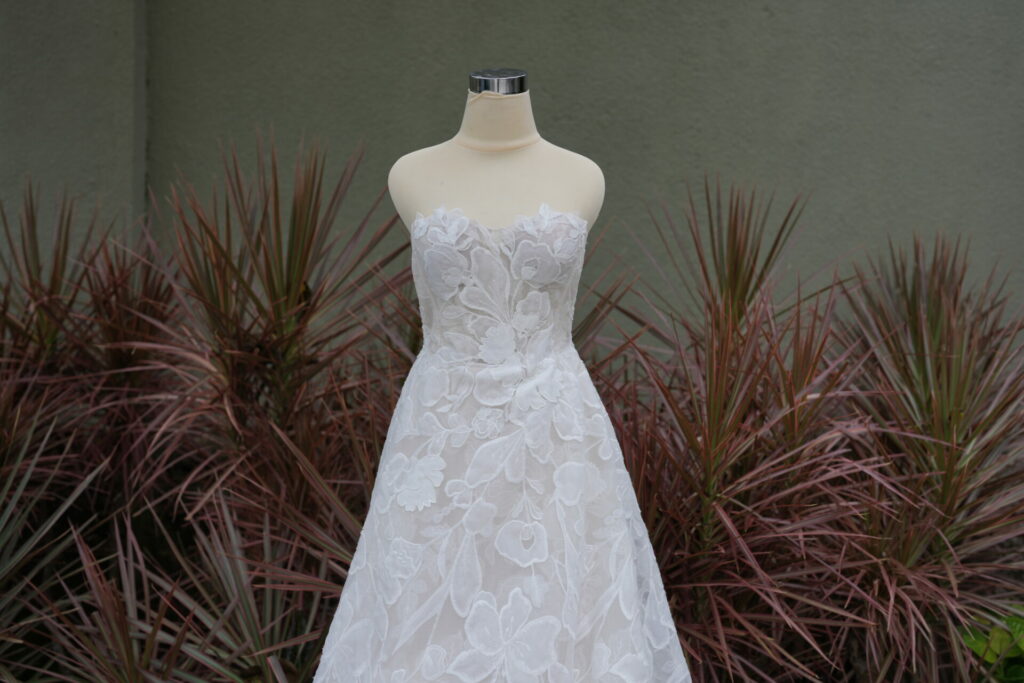 Strapless floral lace wedding dress on mannequin, outdoors.