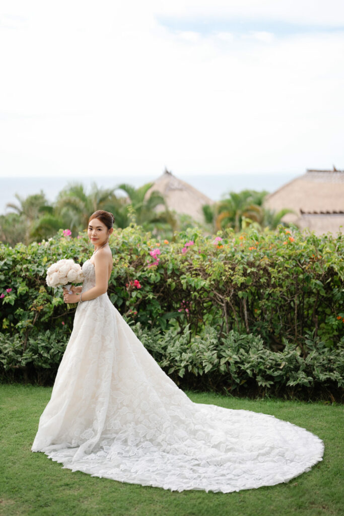 Katya Ruiz in strapless white gown, bouquet, lush garden backdrop.