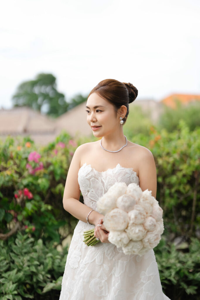 Katya Ruiz smiles in strapless lace gown with bouquet outdoors.