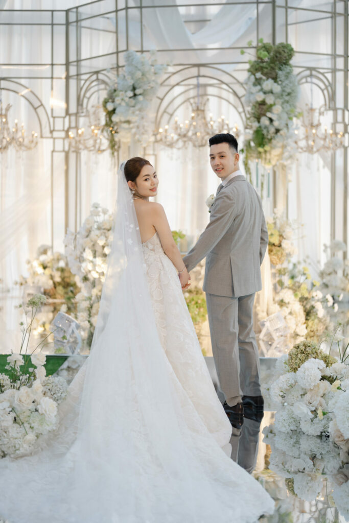 Katya Ruiz and groom smile, holding hands in floral decor.