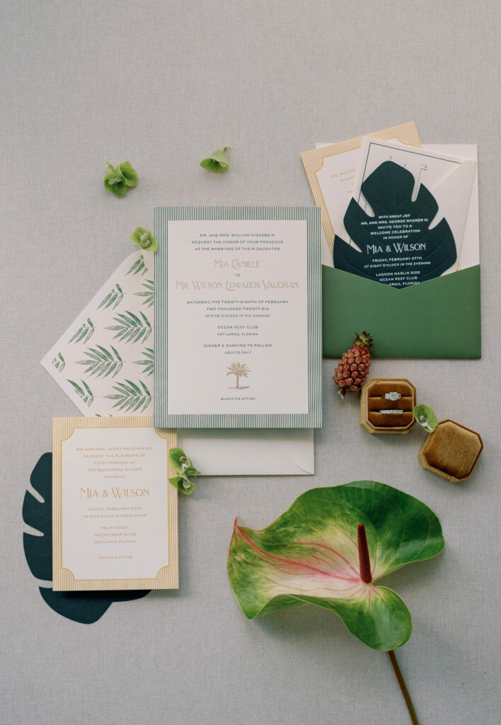 Elegant wedding invitations with tropical accents and rings.