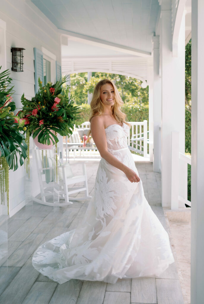 Bride in strapless white lace dress on porch, smiling.