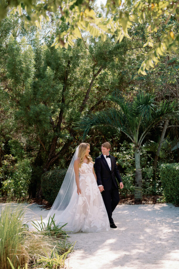 Bride and groom walk together on sunlit garden path.