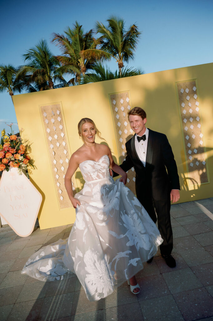Katya Ruiz and groom walk outdoors by yellow walls.