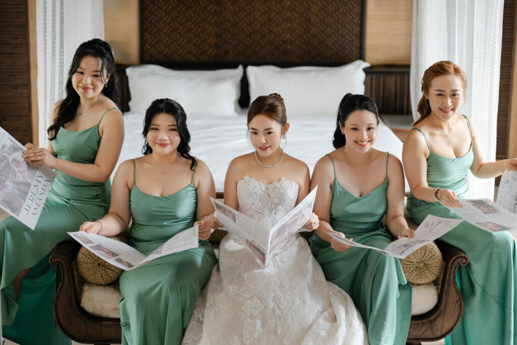 Bride in couture gown sits with four smiling bridesmaids holding newspapers.